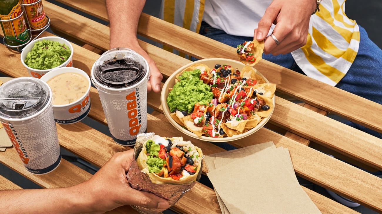 2 people eating a burrito, Nachos and Qdoba drinks